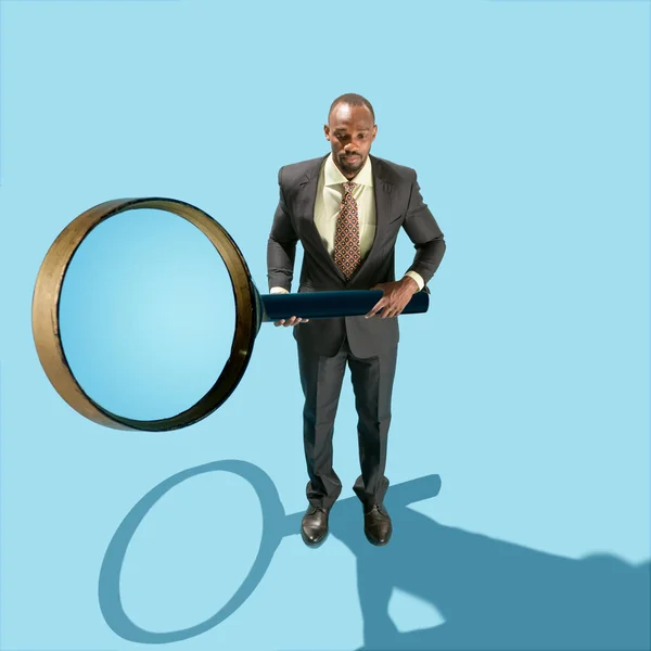 Концептуальний образ бізнесмена, що тримає збільшувальне скло на синьому фоні — стокове фото