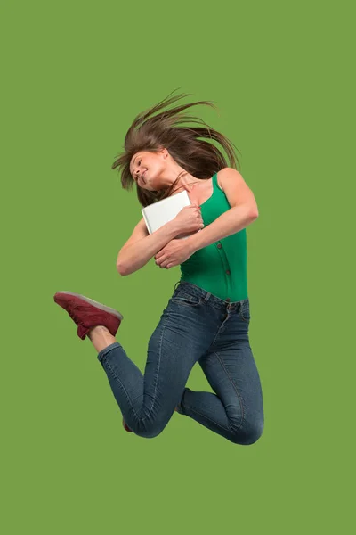 Imagen de mujer joven sobre fondo verde usando computadora portátil o tableta gadget mientras salta . — Foto de Stock