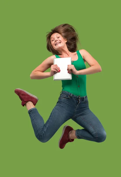 Image of young woman over green background using laptop computer or tablet gadget while jumping. — Stock Photo, Image