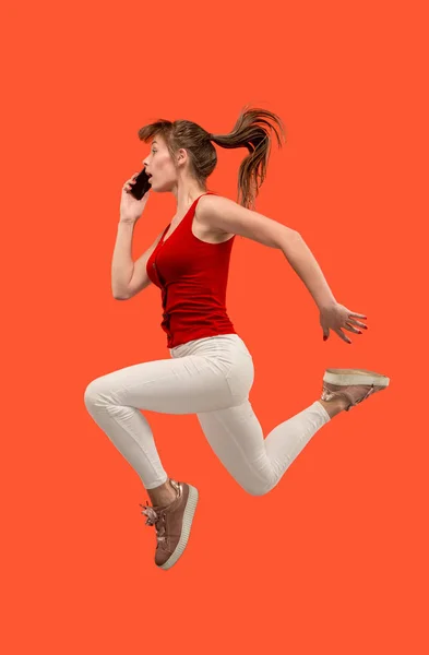 Comprimento total de mulher muito jovem com telefone celular enquanto salta — Fotografia de Stock