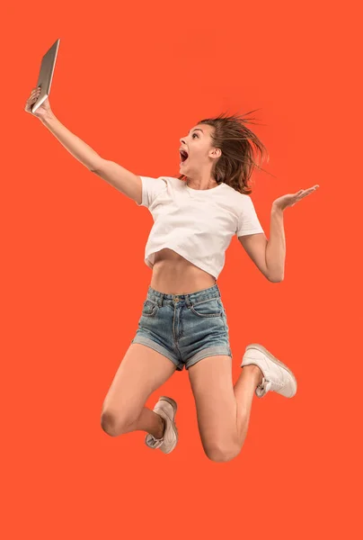 노트북 컴퓨터나 태블릿 가제트를 사용 하 여 점프 하는 동안 빨간색 배경 위에 젊은 여자의 이미지. — 스톡 사진