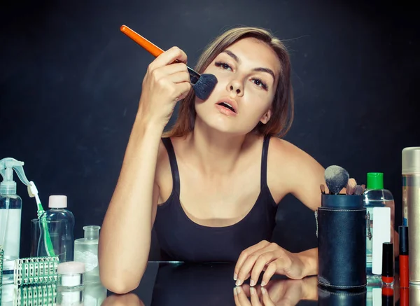 Mulher de beleza aplicando maquiagem. Menina bonita olhando no espelho e aplicando cosméticos com uma escova grande . — Fotografia de Stock