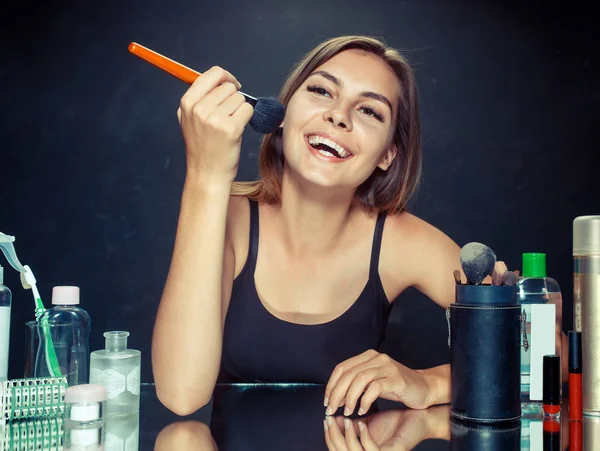 Mujer de belleza aplicando maquillaje. Hermosa chica mirando en el espejo y la aplicación de cosméticos con un cepillo grande . — Foto de Stock