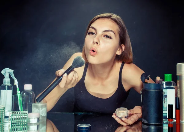 Mujer de belleza aplicando maquillaje. Hermosa chica mirando en el espejo y la aplicación de cosméticos con un cepillo grande . — Foto de Stock