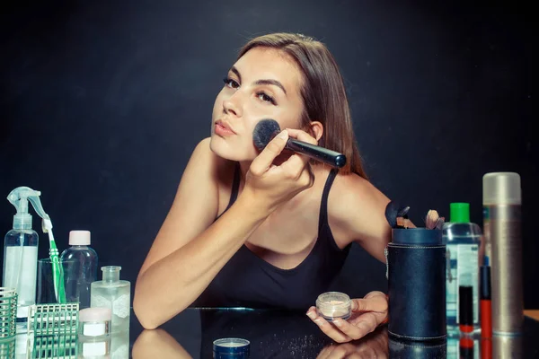 Mulher de beleza aplicando maquiagem. Menina bonita olhando no espelho e aplicando cosméticos com uma escova grande . — Fotografia de Stock