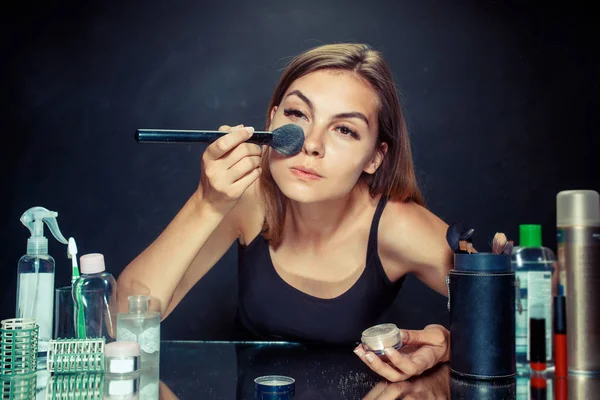 Mulher de beleza aplicando maquiagem. Menina bonita olhando no espelho e aplicando cosméticos com uma escova grande . — Fotografia de Stock