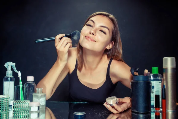 Mulher de beleza aplicando maquiagem. Menina bonita olhando no espelho e aplicando cosméticos com uma escova grande . — Fotografia de Stock