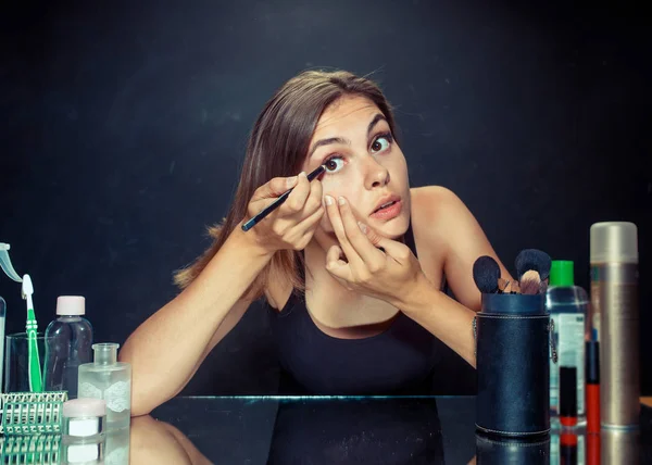 Mulher de beleza aplicando maquiagem. Menina bonita olhando no espelho e aplicando cosméticos com uma escova . — Fotografia de Stock