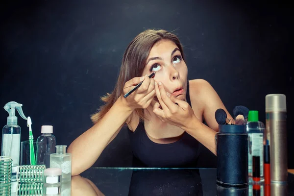 Mujer de belleza aplicando maquillaje. Hermosa chica mirando en el espejo y la aplicación de cosméticos con un cepillo . — Foto de Stock