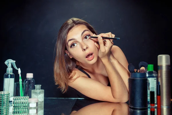 Mulher de beleza aplicando maquiagem. Menina bonita olhando no espelho e aplicando cosméticos com uma escova . — Fotografia de Stock