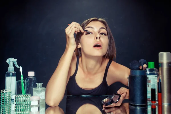 Mujer de belleza aplicando maquillaje. Hermosa chica mirando en el espejo y la aplicación de cosméticos con un cepillo . — Foto de Stock