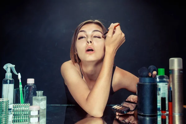 Mulher de beleza aplicando maquiagem. Menina bonita olhando no espelho e aplicando cosméticos com uma escova . — Fotografia de Stock