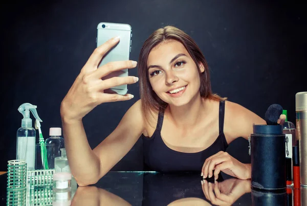 Красавица с макияжем. Красивая девушка смотрит на мобильный телефон и делает селфи фото — стоковое фото