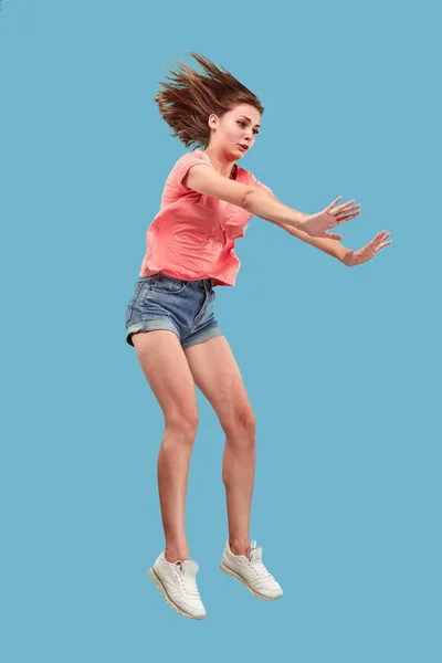 Freedom in moving. Pretty young woman jumping against blue background — Stock Photo, Image