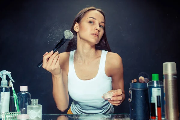 Mujer de belleza aplicando maquillaje. Hermosa chica mirando en el espejo y la aplicación de cosméticos con un cepillo grande . — Foto de Stock