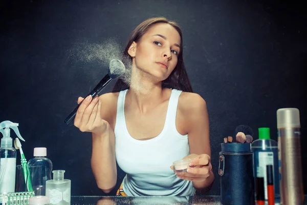 Mulher de beleza aplicando maquiagem. Menina bonita olhando no espelho e aplicando cosméticos com uma escova grande . — Fotografia de Stock