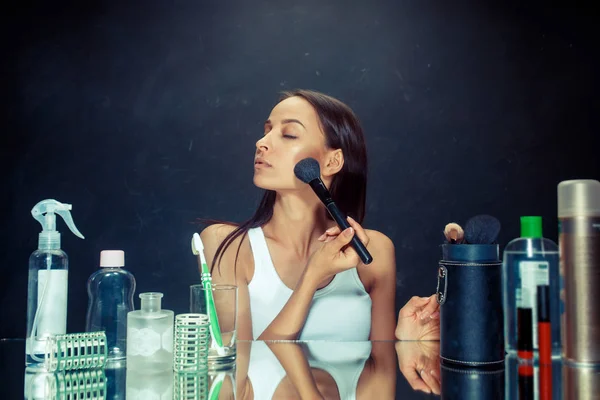 Mulher de beleza aplicando maquiagem. Menina bonita olhando no espelho e aplicando cosméticos com uma escova grande . — Fotografia de Stock