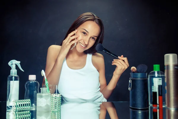 Mujer de belleza aplicando maquillaje. Hermosa chica mirando en el espejo y la aplicación de cosméticos con un cepillo grande . — Foto de Stock