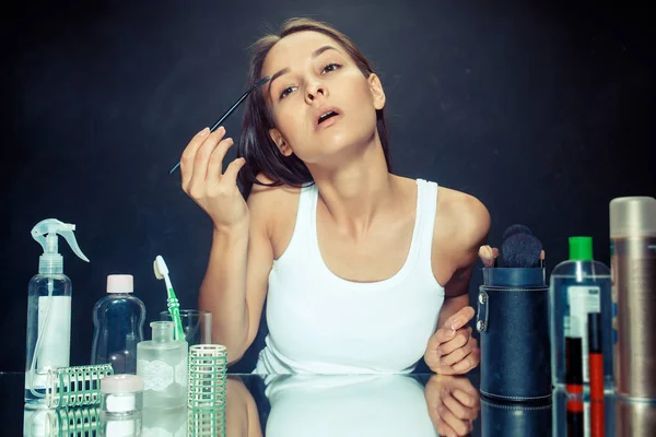 Mujer de belleza aplicando maquillaje. Hermosa chica mirando en el espejo y la aplicación de cosméticos con un cepillo . — Foto de Stock