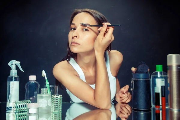 Mujer de belleza aplicando maquillaje. Hermosa chica mirando en el espejo y la aplicación de cosméticos con un cepillo . — Foto de Stock