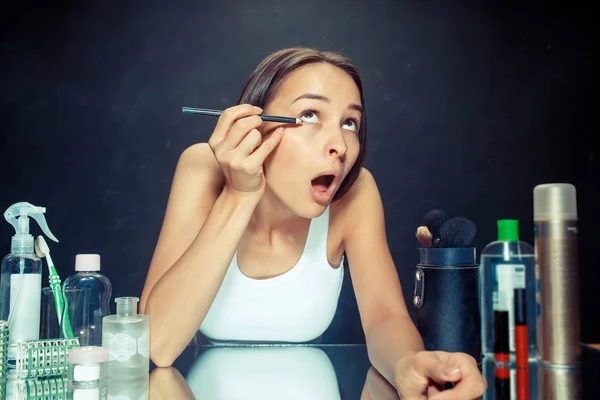 Mujer de belleza aplicando maquillaje. Hermosa chica mirando en el espejo y la aplicación de cosméticos con un lápiz de ojos . — Foto de Stock