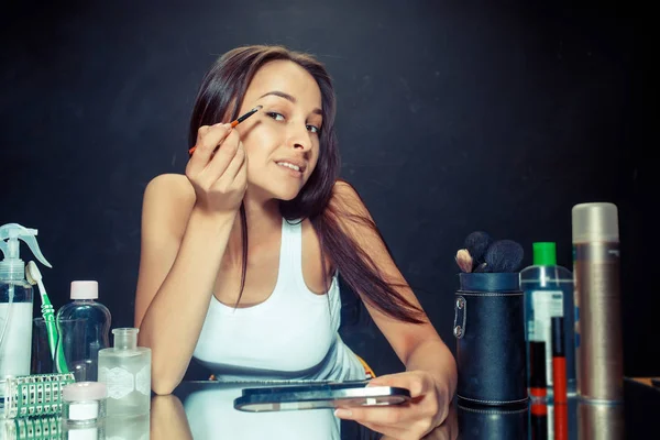 Mulher de beleza aplicando maquiagem. Menina bonita olhando no espelho e aplicando cosméticos com uma escova . — Fotografia de Stock