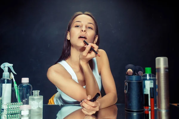Mujer de belleza aplicando maquillaje. Hermosa chica mirando en el espejo y la aplicación de cosméticos con un cepillo . — Foto de Stock