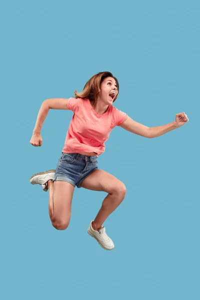 Freiheit in der Bewegung. hübsche junge Frau springt vor blauem Hintergrund — Stockfoto
