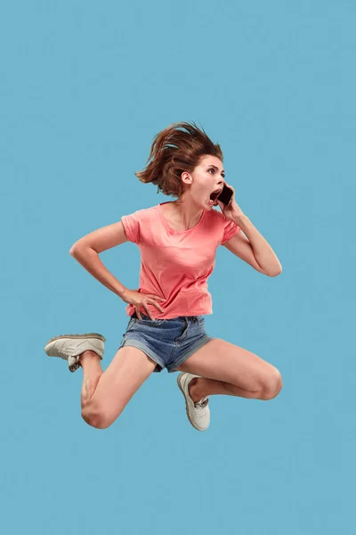 Comprimento total de mulher muito jovem com telefone celular enquanto salta — Fotografia de Stock