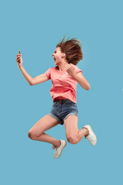 Longitud completa de la mujer joven y bonita con teléfono móvil mientras salta — Foto de Stock