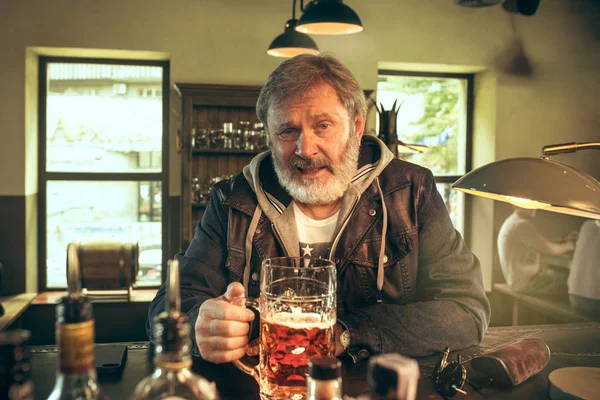 Старший бородатый мужчина пьет пиво в пабе — стоковое фото