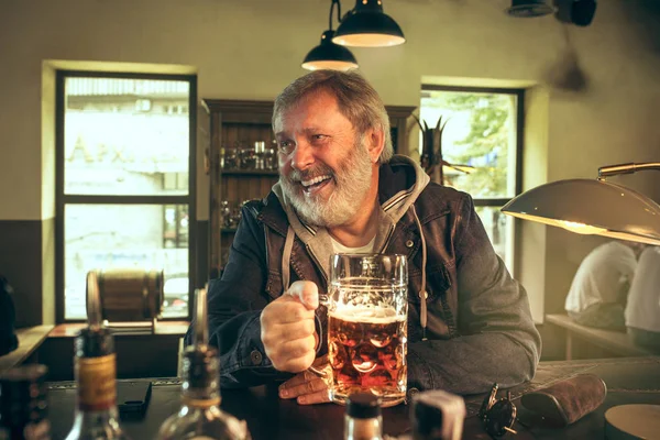 Der ältere bärtige Mann trinkt Bier in der Kneipe — Stockfoto