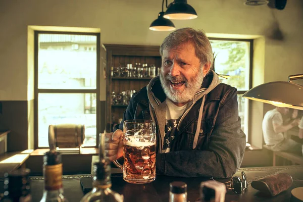 Der ältere bärtige Mann trinkt Bier in der Kneipe — Stockfoto