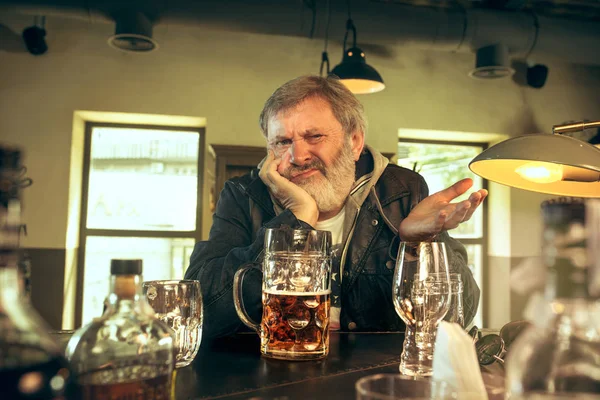 De trieste senior gebaarde mannelijke drinken bier in de kroeg — Stockfoto