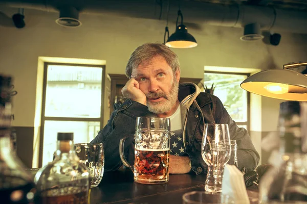 Грустный бородатый мужчина, пьющий пиво в пабе — стоковое фото
