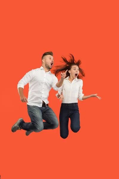 Frihet i rörelse. Förvånade unga paret hoppa mot röd bakgrund — Stockfoto