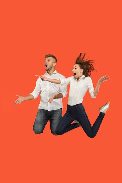 Libertad de movimiento. Sorprendida joven pareja saltando sobre fondo rojo — Foto de Stock