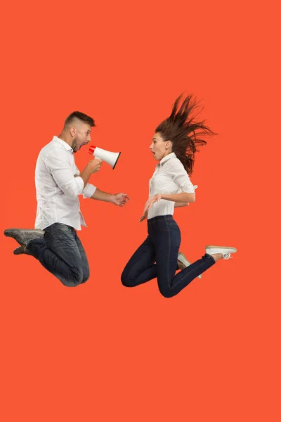 Güzel genç çift kırmızı arka plan üzerinde izole megafon ile atlama — Stok fotoğraf