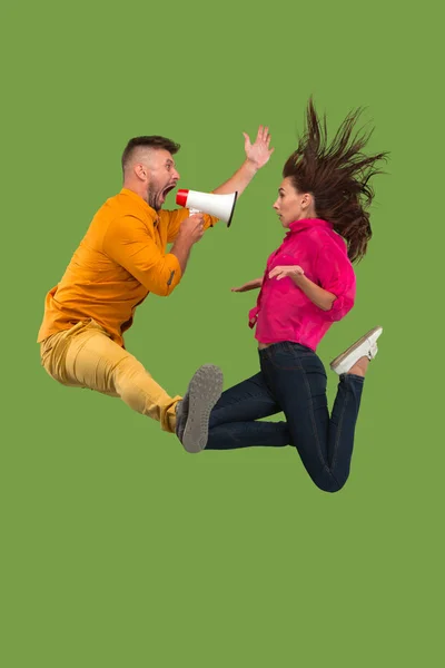 Belo jovem casal pulando com megafone isolado sobre fundo verde — Fotografia de Stock