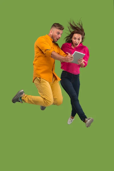 Hoppa av ungt par över gröna studio bakgrund med bärbar dator eller surfplatta gadget medan hoppning. — Stockfoto