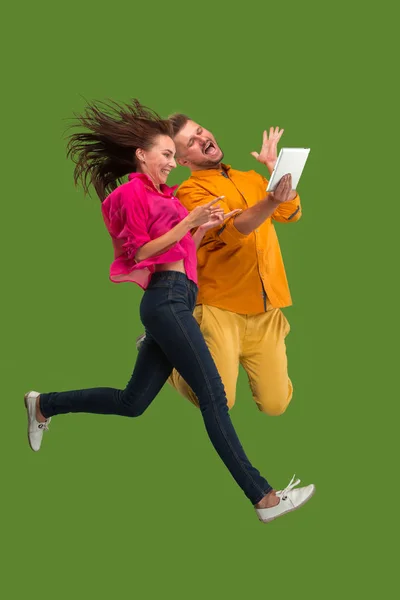 Salto di giovane coppia su sfondo rosso studio utilizzando laptop o tablet gadget durante il salto . — Foto Stock