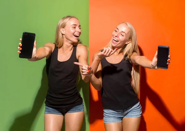 Portrait of a confident casual girls showing blank screen mobile phone isolated over colorful background — Stock Photo, Image