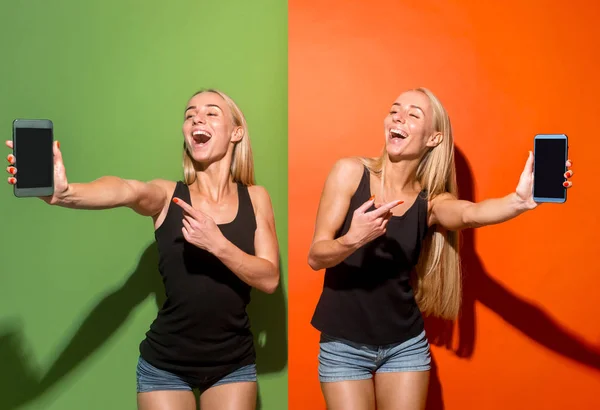 Portrait of a confident casual girls showing blank screen mobile phone isolated over colorful background — Stock Photo, Image