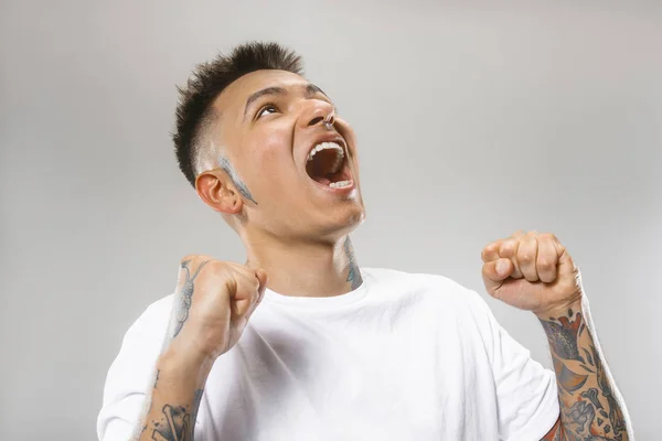 Молодой эмоциональный сердитый мужчина кричит на фоне серой студии — стоковое фото