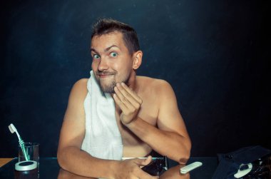 Yatak odası oturma sakalını tırmalamak aynanın önünde genç adam