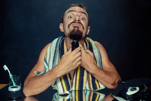 Jovem no quarto sentado na frente do espelho coçando sua barba — Fotografia de Stock