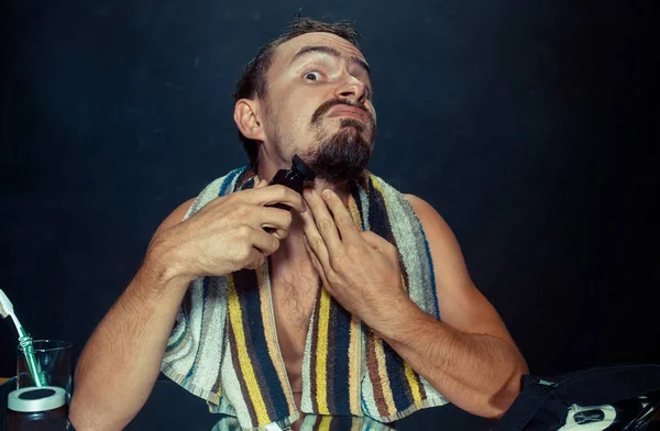 Jovem no quarto sentado na frente do espelho coçando sua barba — Fotografia de Stock