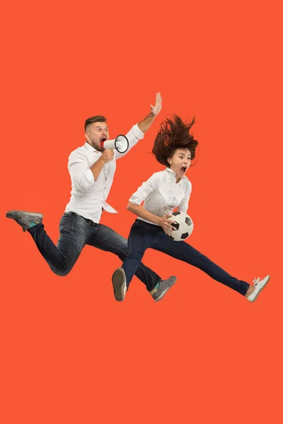 Forward to the victory.The young couple as soccer football player jumping and kicking the ball at studio on a red — Stock Photo, Image