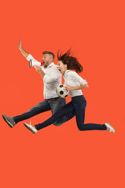 Forward to the victory.The young couple as soccer football player jumping and kicking the ball at studio on a red — Stock Photo, Image
