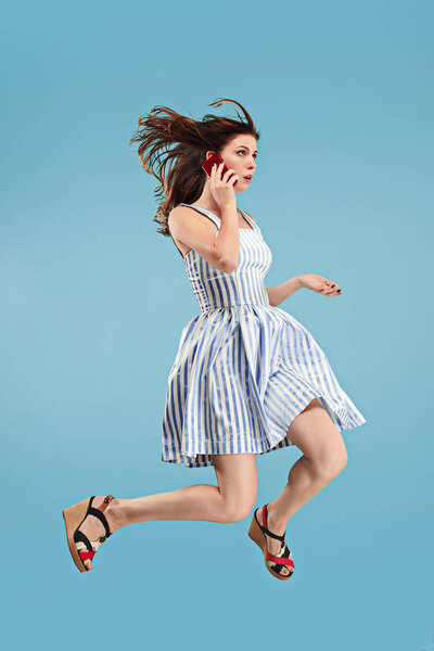 Полная длина симпатичной молодой женщины с мобильным телефоном во время прыжка
